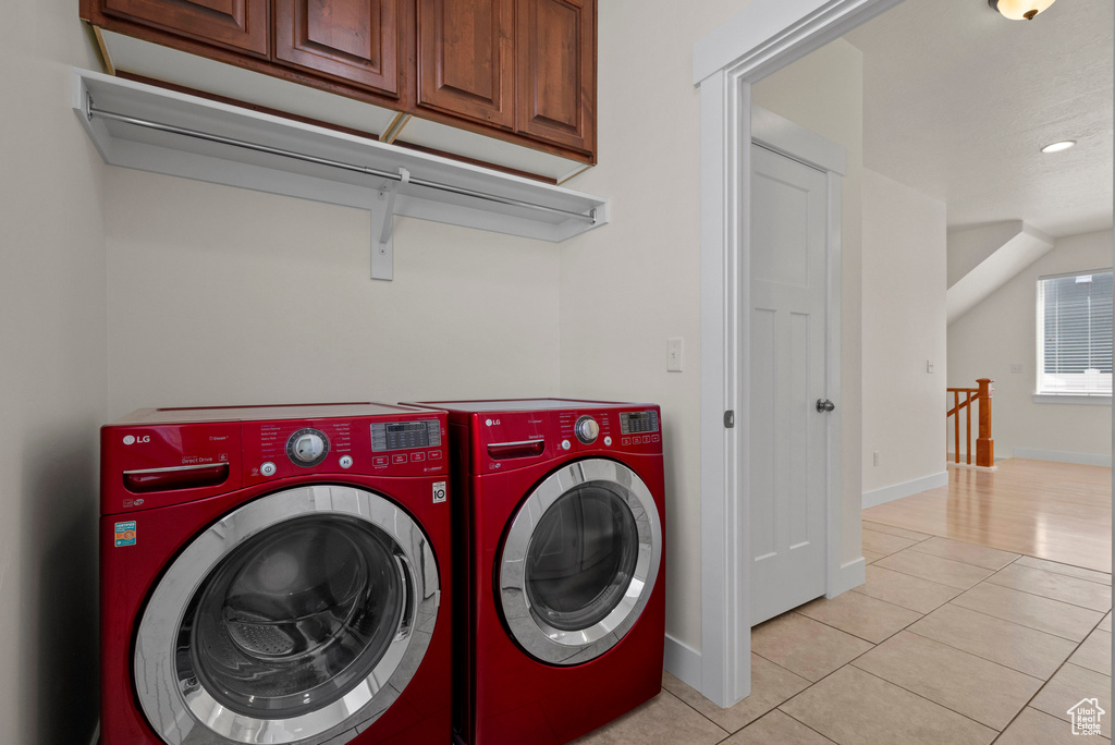 Laundry room featuring separate washer and dryer, cabinet space, light tile patterned floors, and baseboards