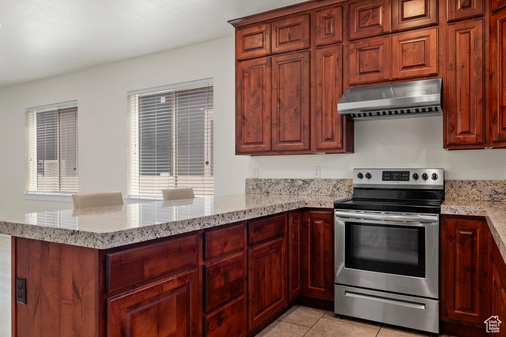Kitchen featuring under cabinet range hood, stainless steel range with electric stovetop, a peninsula, light stone counters, and light tile patterned floors
