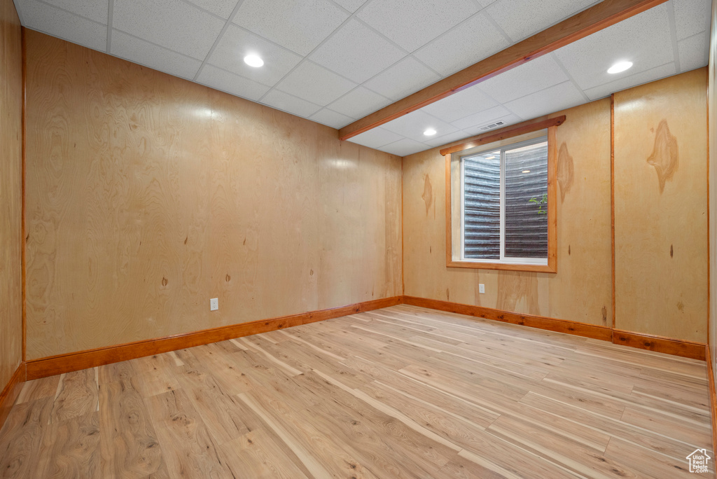 Empty room with light wood-type flooring, a drop ceiling, recessed lighting, baseboards, and wooden walls