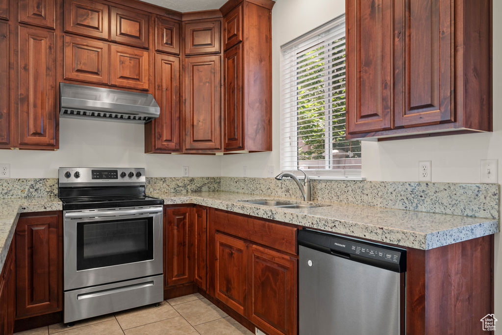 Kitchen featuring appliances with stainless steel finishes, under cabinet range hood, a sink, light tile patterned floors, and light stone counters
