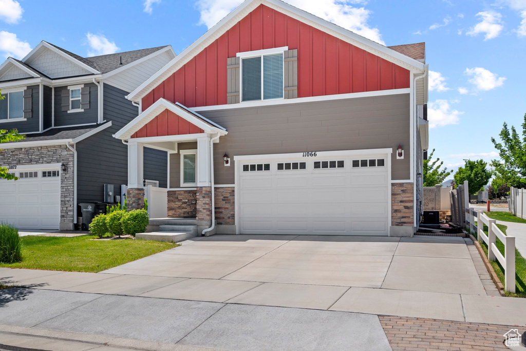 Craftsman-style home with board and batten siding, stone siding, a garage, and driveway