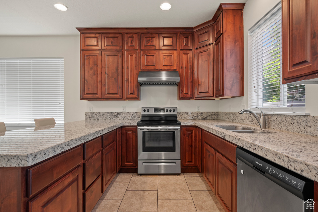Kitchen with appliances with stainless steel finishes, a sink, under cabinet range hood, a peninsula, and light tile patterned floors
