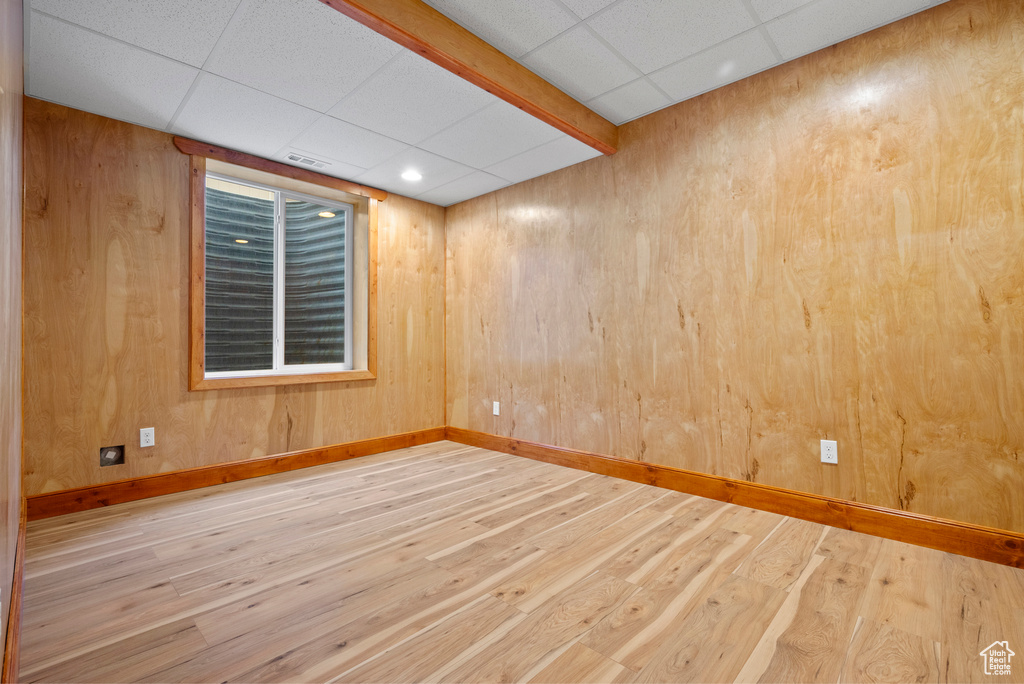 Unfurnished room featuring a drop ceiling, wood finished floors, baseboards, and wooden walls