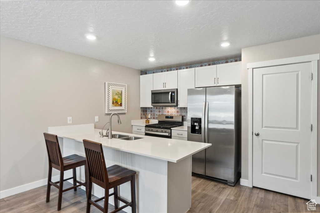 Kitchen featuring appliances with stainless steel finishes, a sink, a kitchen bar, wood finished floors, and a peninsula