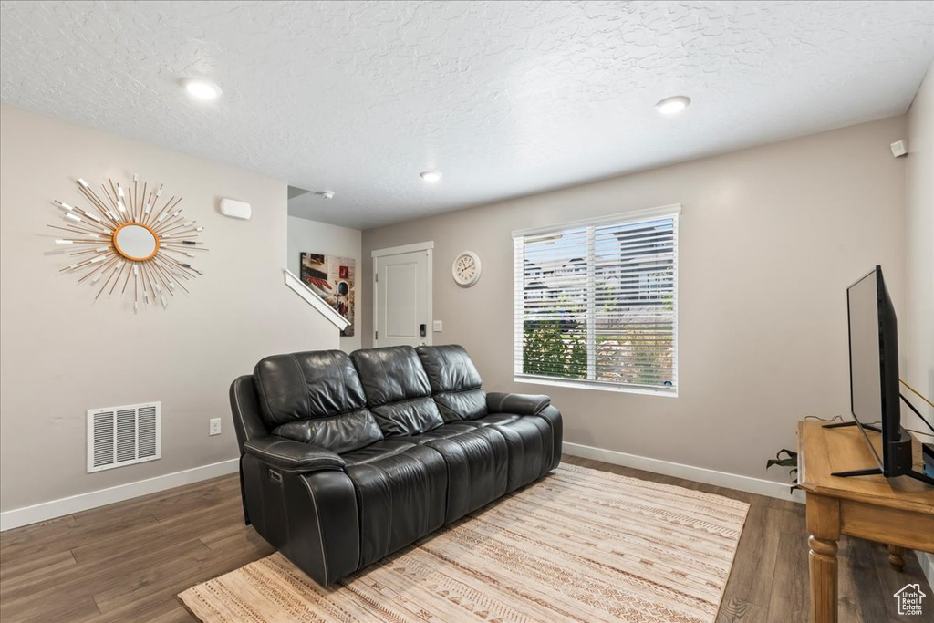 Living room with baseboards, wood finished floors, a textured ceiling, and recessed lighting