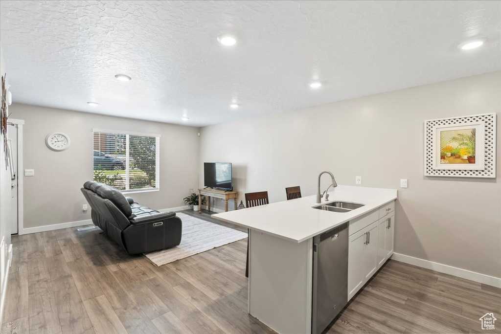 Kitchen featuring stainless steel dishwasher, a sink, a peninsula, open floor plan, and wood finished floors