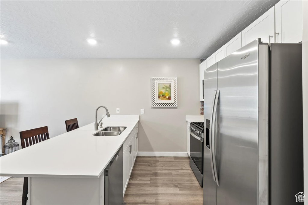 Kitchen featuring stainless steel appliances, a sink, a peninsula, a breakfast bar, and light wood-style floors