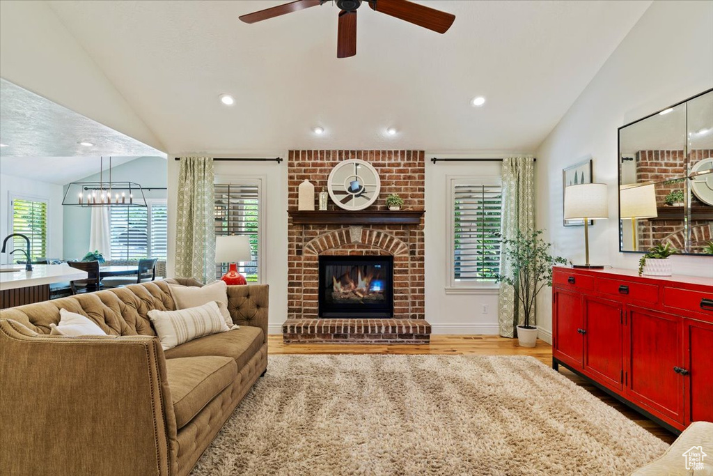 Living area featuring vaulted ceiling, light wood-style flooring, ceiling fan, recessed lighting, and a fireplace