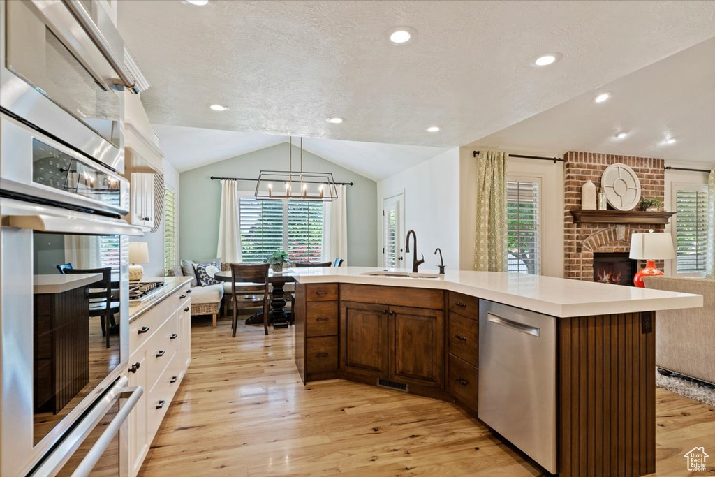 Kitchen featuring stainless steel appliances, a sink, light wood-type flooring, vaulted ceiling, and a chandelier