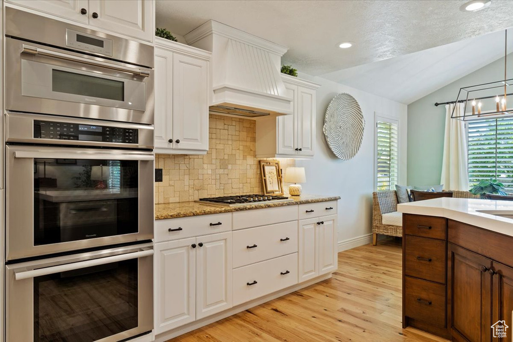 Kitchen featuring lofted ceiling, light wood-type flooring, decorative backsplash, stainless steel appliances, and white cabinets