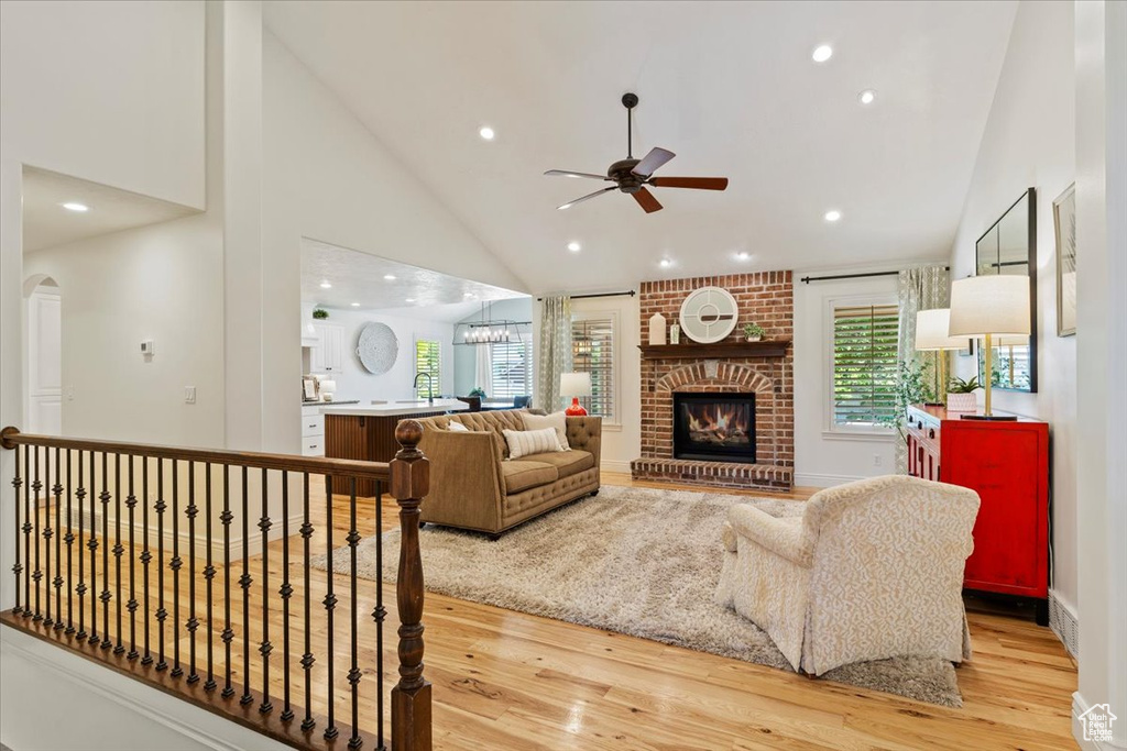 Living room featuring ceiling fan, light wood-style flooring, high vaulted ceiling, a fireplace, and recessed lighting