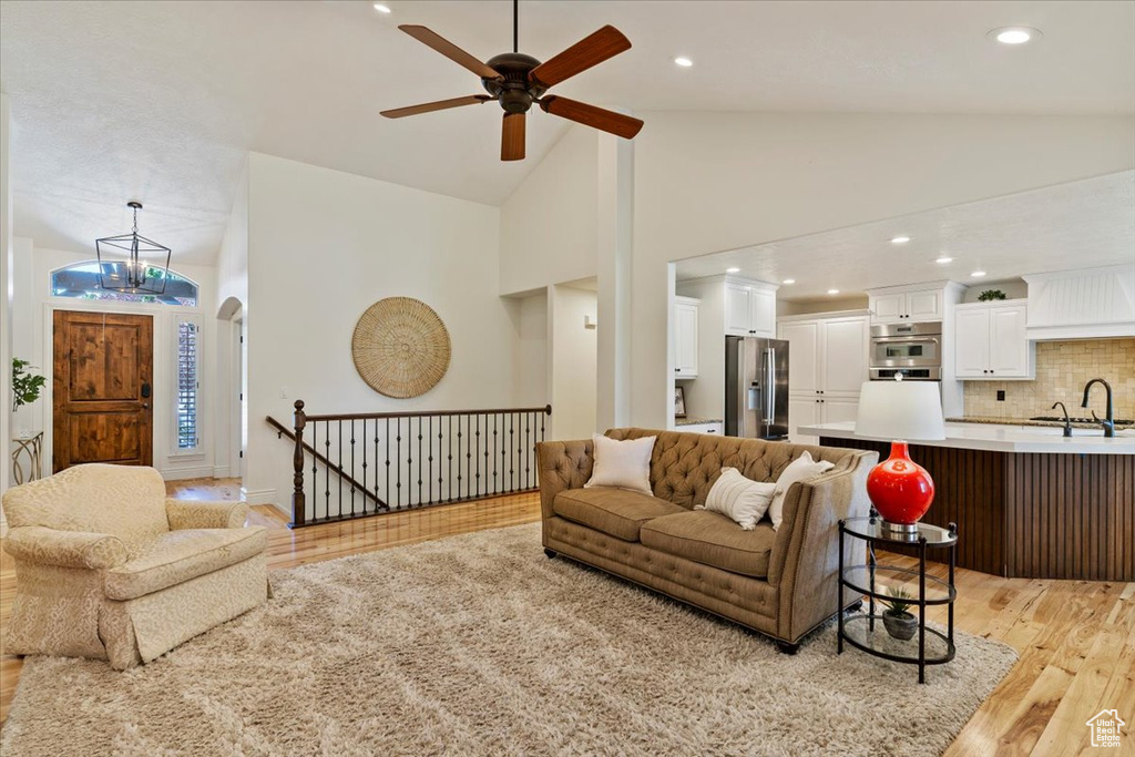 Living room with light wood finished floors, a ceiling fan, high vaulted ceiling, and recessed lighting