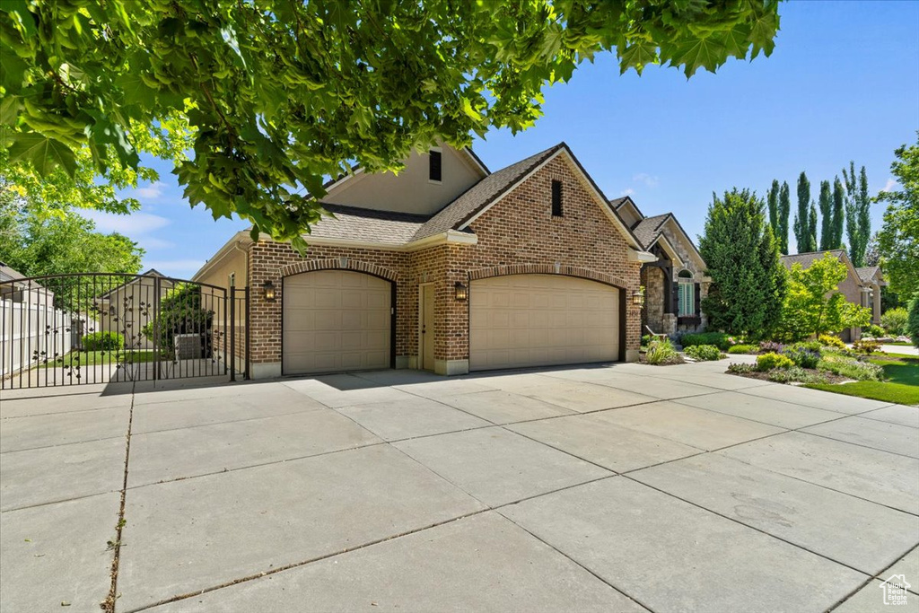 View of front facade with concrete driveway, an attached garage, brick siding, and a gate