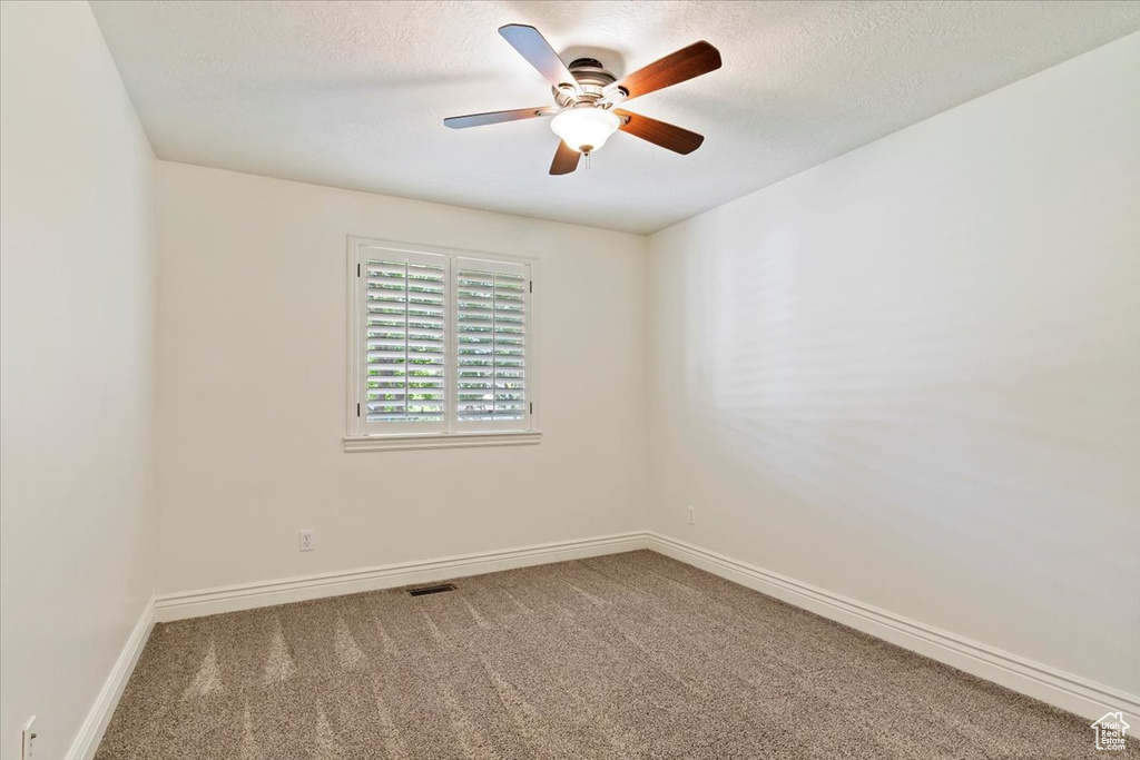 Carpeted empty room with a textured ceiling, baseboards, and a ceiling fan