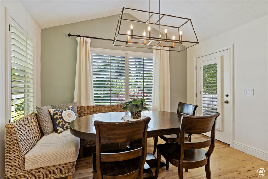 Dining space featuring plenty of natural light, light wood finished floors, a chandelier, vaulted ceiling, and baseboards