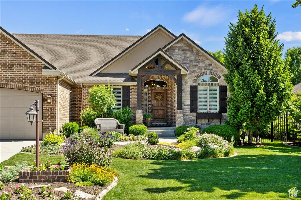 View of front of property featuring brick siding, a front lawn, roof with shingles, an attached garage, and driveway