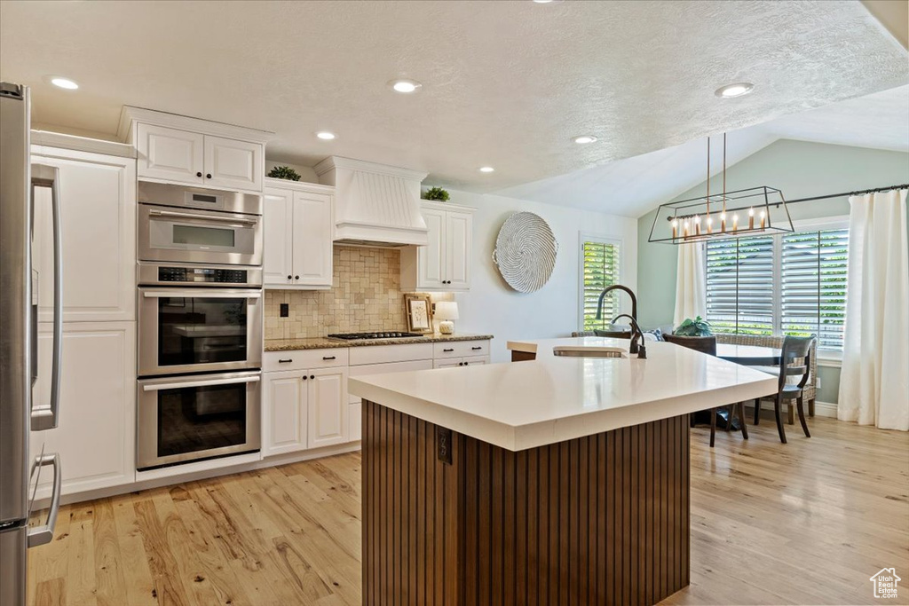 Kitchen featuring appliances with stainless steel finishes, light wood-style flooring, premium range hood, a chandelier, and a sink