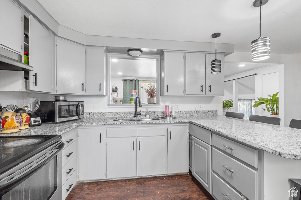 Kitchen featuring a sink, appliances with stainless steel finishes, a peninsula, light stone counters, and hanging light fixtures