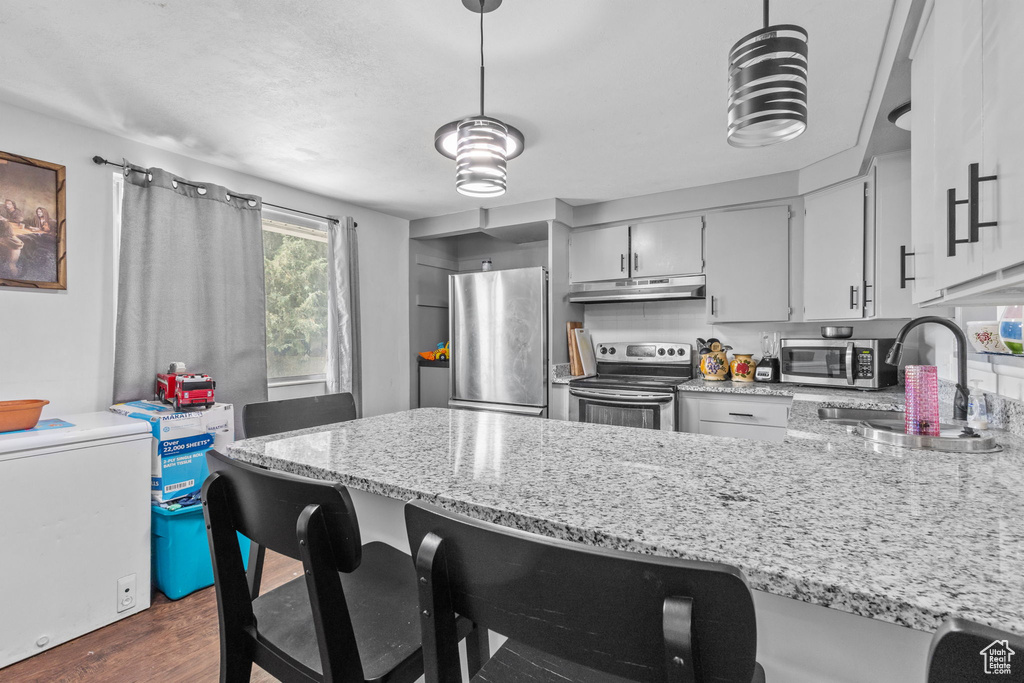 Kitchen with stainless steel appliances, under cabinet range hood, a sink, light stone counters, and a peninsula