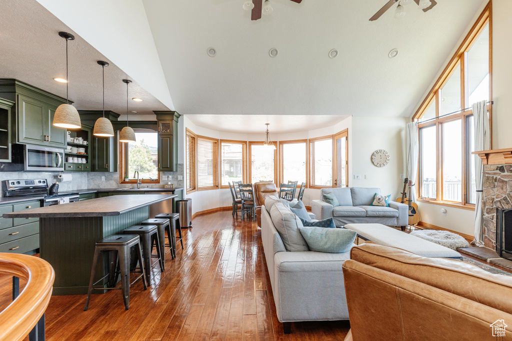 Living room featuring ceiling fan, baseboards, high vaulted ceiling, dark wood finished floors, and a stone fireplace