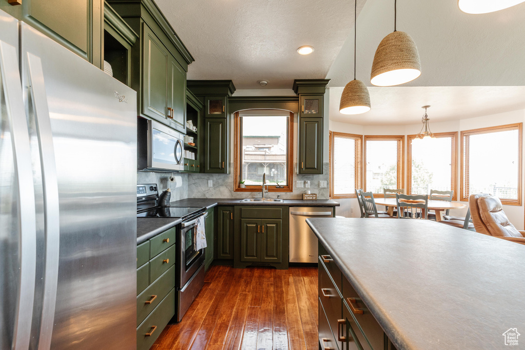 Kitchen featuring appliances with stainless steel finishes, green cabinetry, dark wood-style flooring, tasteful backsplash, and a sink