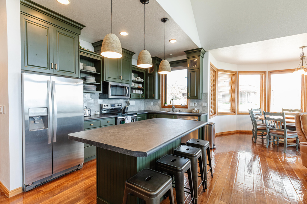 Kitchen featuring stainless steel appliances, green cabinets, open shelves, dark countertops, and baseboards