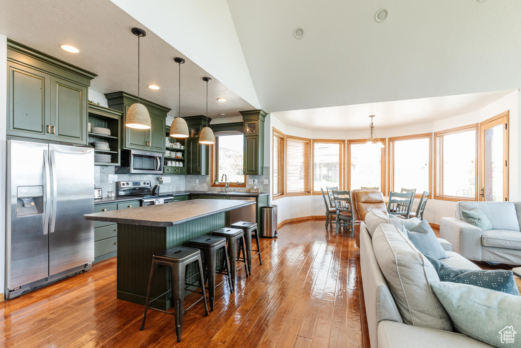 Kitchen with green cabinetry, stainless steel appliances, open shelves, open floor plan, and dark countertops