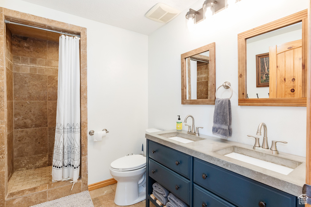 Full bath featuring double vanity, toilet, a tile shower, and tile patterned flooring