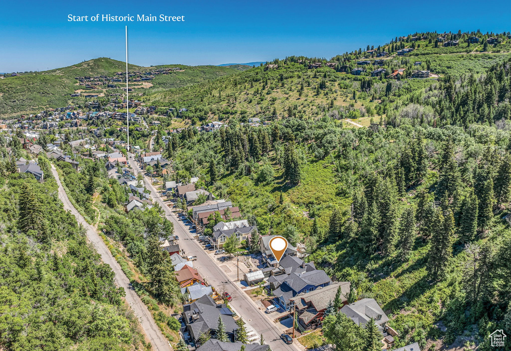 Aerial view of property and surrounding area with a heavily wooded area, mountains, and nearby suburban area