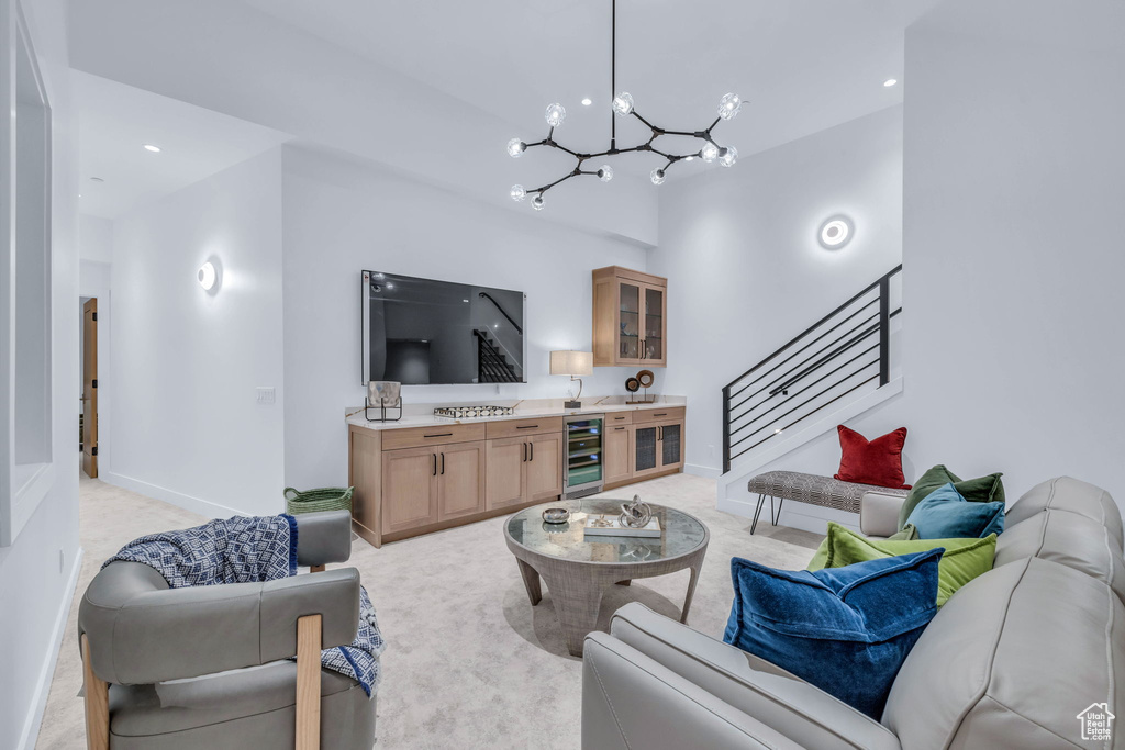 Living room with a chandelier, wine cooler, light carpet, stairs, and baseboards