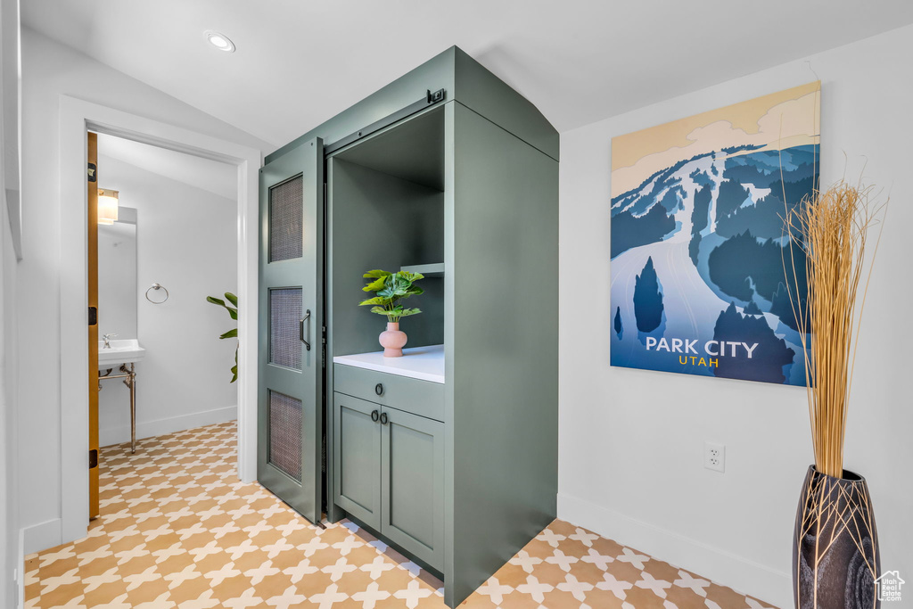 Hall featuring vaulted ceiling, baseboards, and tile patterned floors