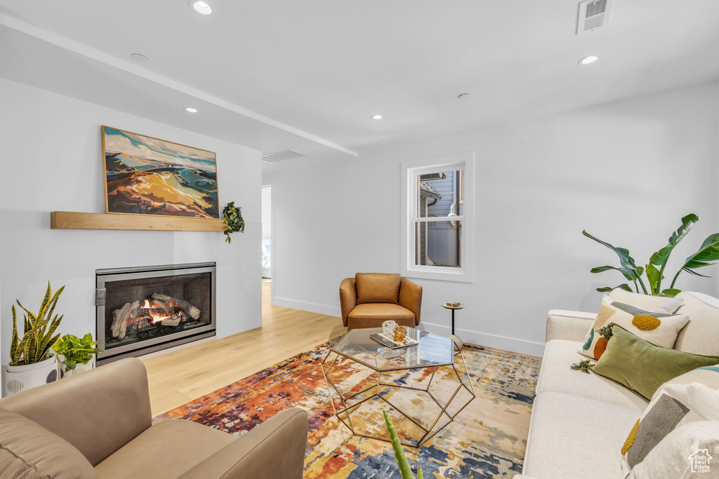 Living room with wood finished floors, recessed lighting, a warm lit fireplace, and baseboards