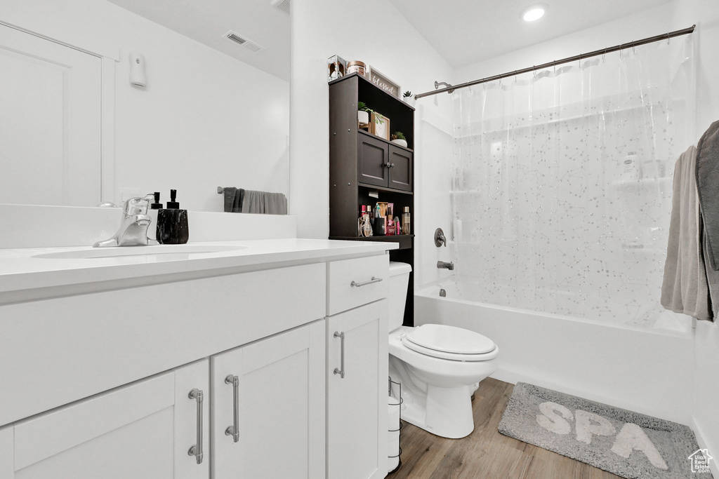 Bathroom featuring vanity, shower / tub combo with curtain, toilet, wood finished floors, and recessed lighting