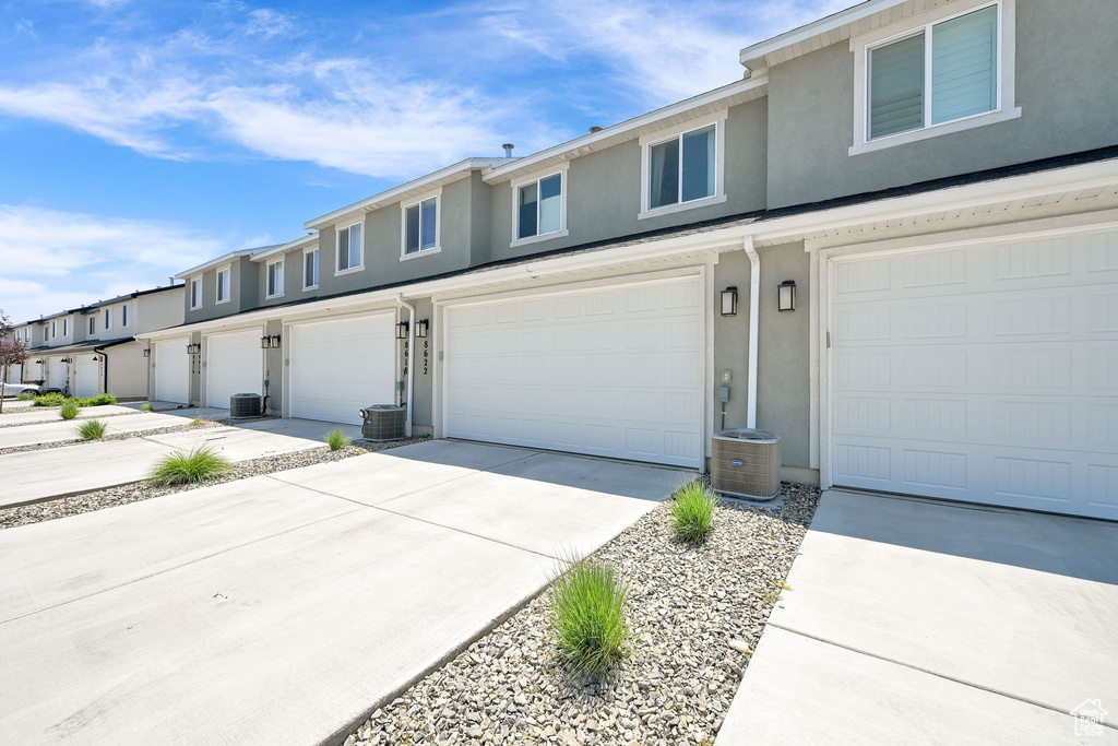 Multi unit property with stucco siding, an attached garage, driveway, and central air condition unit