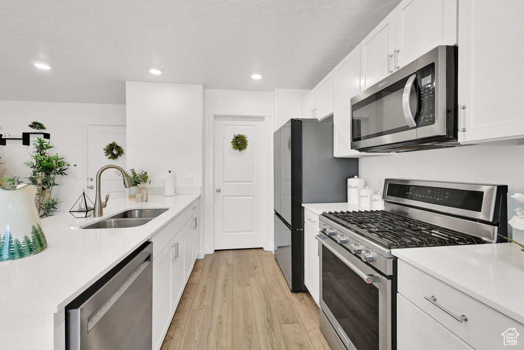 Kitchen with stainless steel appliances, a sink, light wood finished floors, white cabinetry, and light countertops