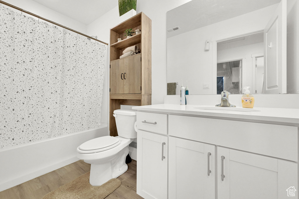 Bathroom with vanity, toilet, wood finished floors, and shower / bathtub combination with curtain