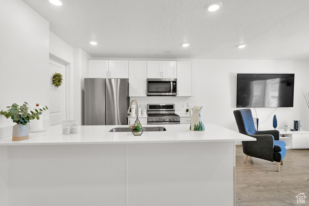 Kitchen with appliances with stainless steel finishes, a sink, white cabinets, a peninsula, and recessed lighting