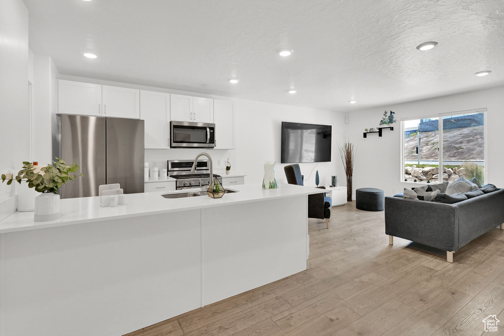 Kitchen featuring appliances with stainless steel finishes, light wood finished floors, light countertops, a sink, and recessed lighting