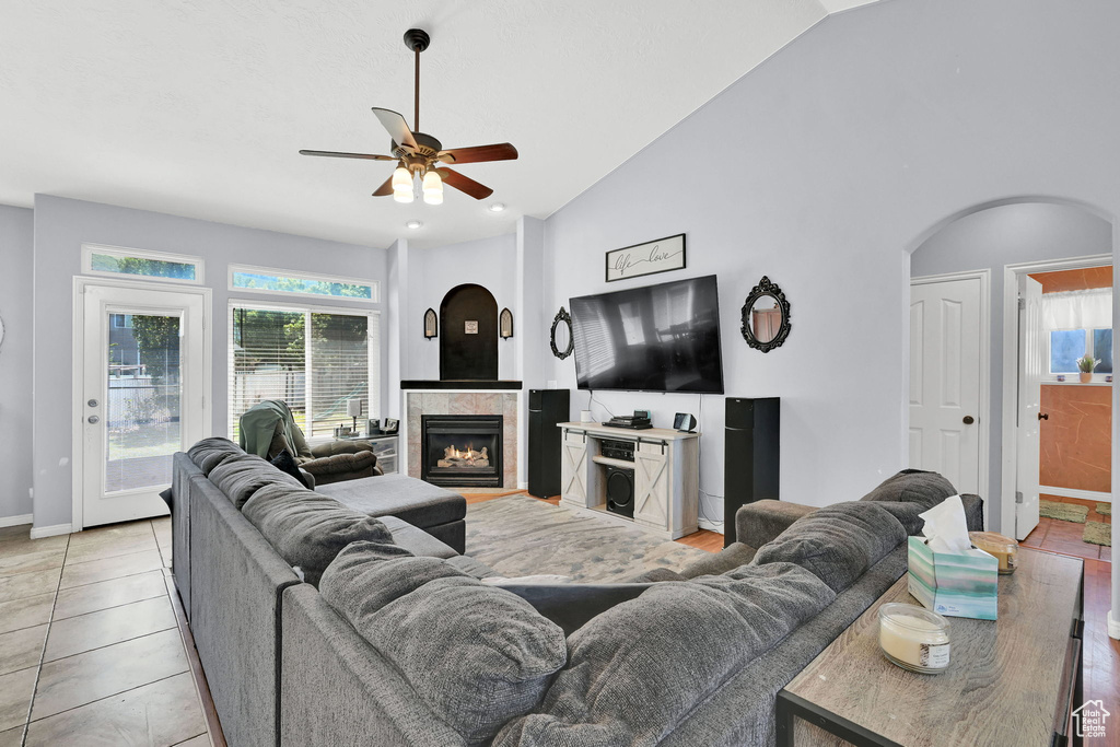 Living room featuring ceiling fan, arched walkways, a fireplace, baseboards, and light tile patterned floors