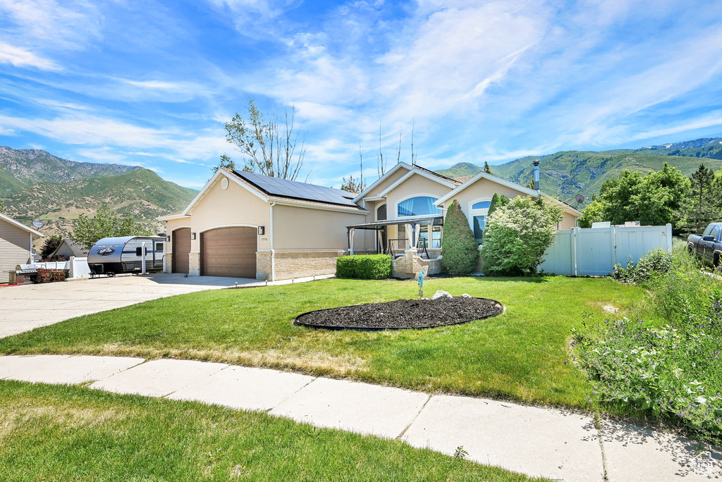 Ranch-style house featuring stucco siding, a mountain view, driveway, roof mounted solar panels, and a garage