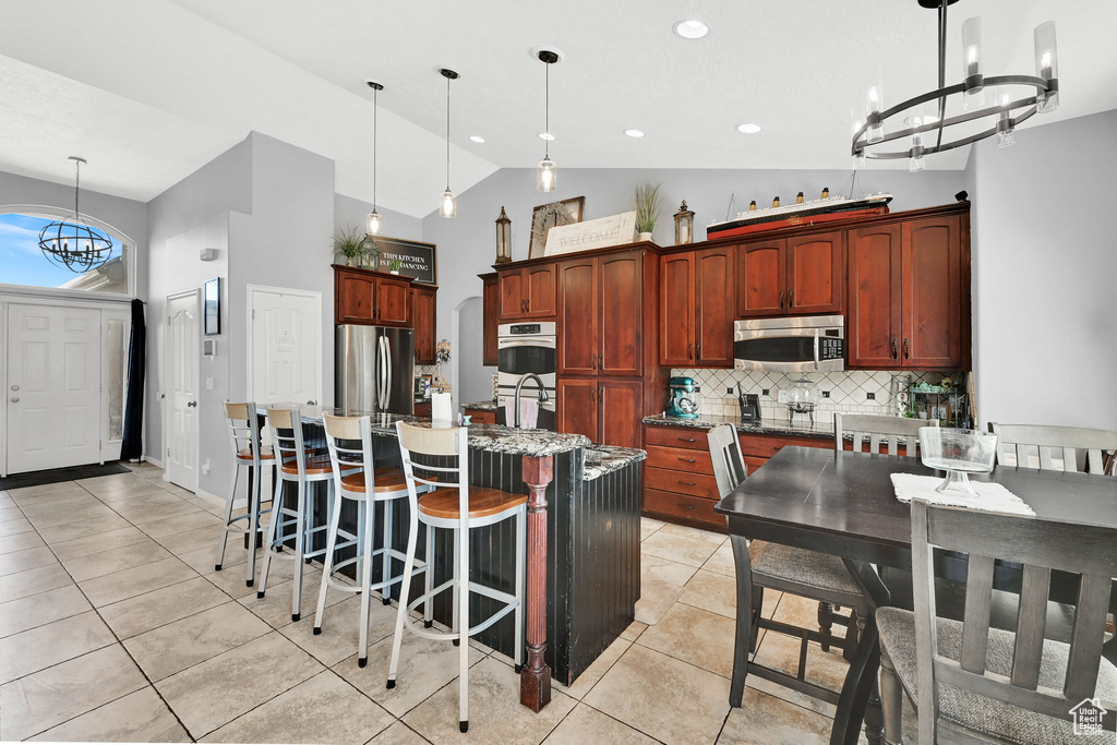 Kitchen featuring stainless steel appliances, a chandelier, decorative backsplash, an island with sink, and light tile patterned floors