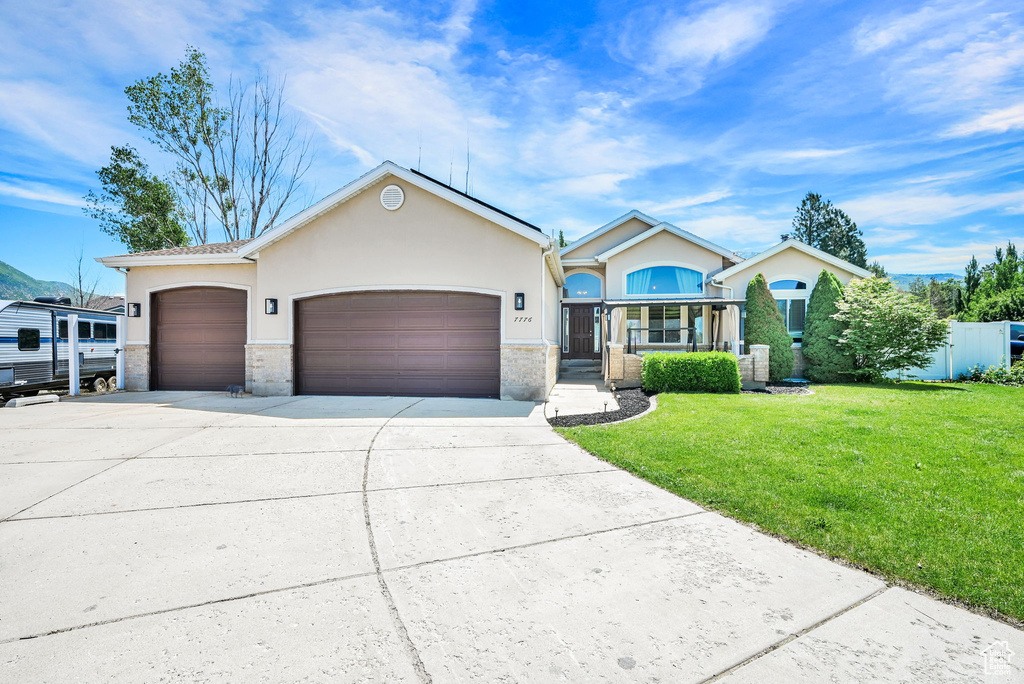 Ranch-style house featuring driveway, an attached garage, stucco siding, a front yard, and brick siding