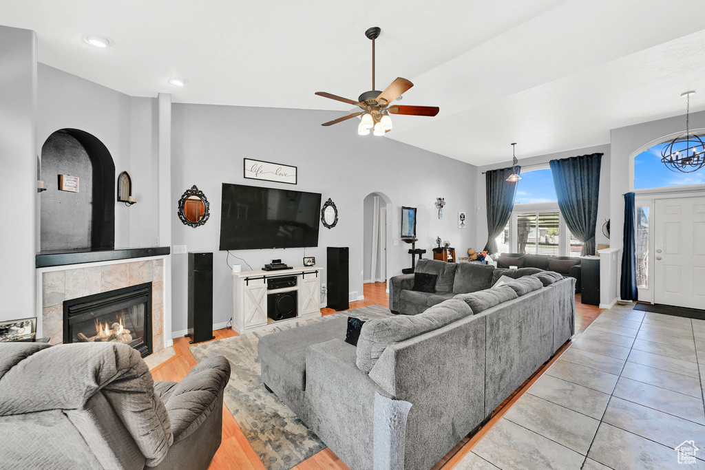 Living area with arched walkways, a tiled fireplace, vaulted ceiling, a ceiling fan, and recessed lighting
