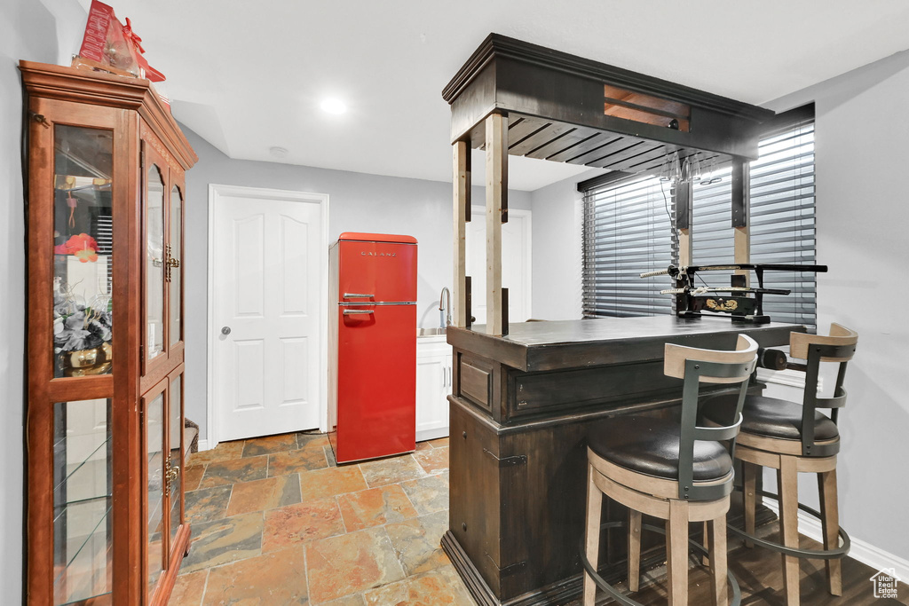 Indoor bar featuring refrigerator, stone tile floors, baseboards, and recessed lighting