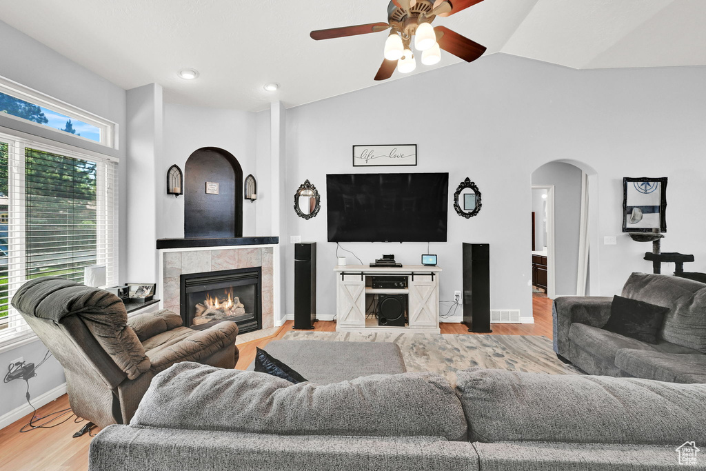 Living area with arched walkways, plenty of natural light, ceiling fan, a tiled fireplace, and lofted ceiling