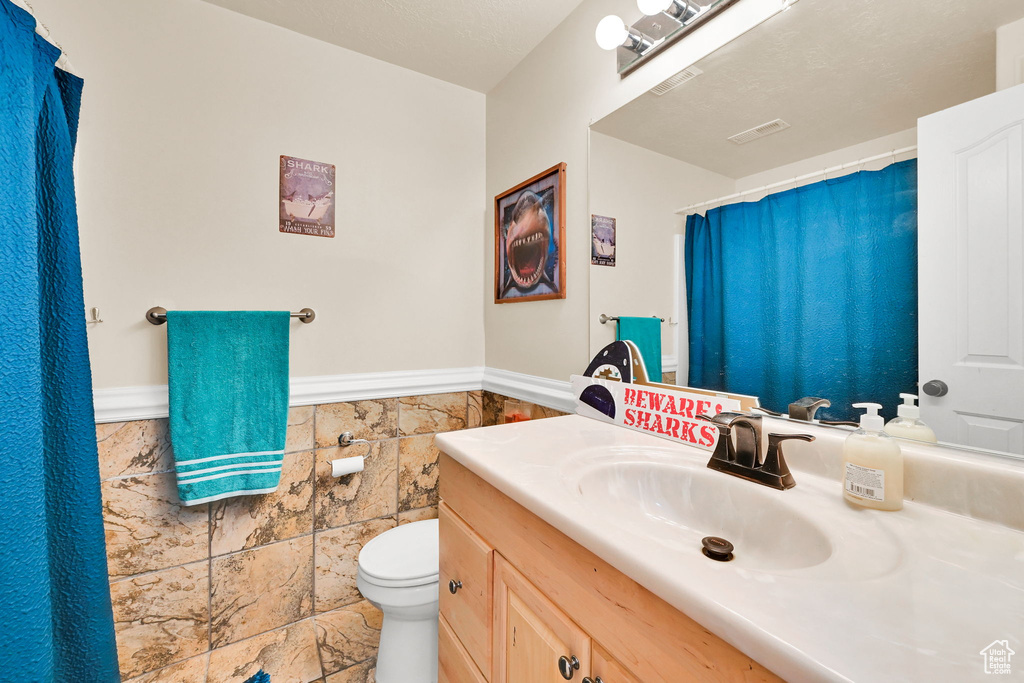 Full bathroom with vanity, wainscoting, toilet, and tile walls