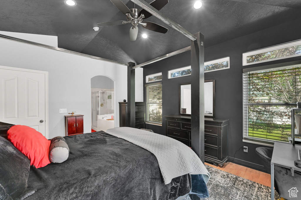 Bedroom featuring wood finished floors, arched walkways, recessed lighting, vaulted ceiling, and connected bathroom