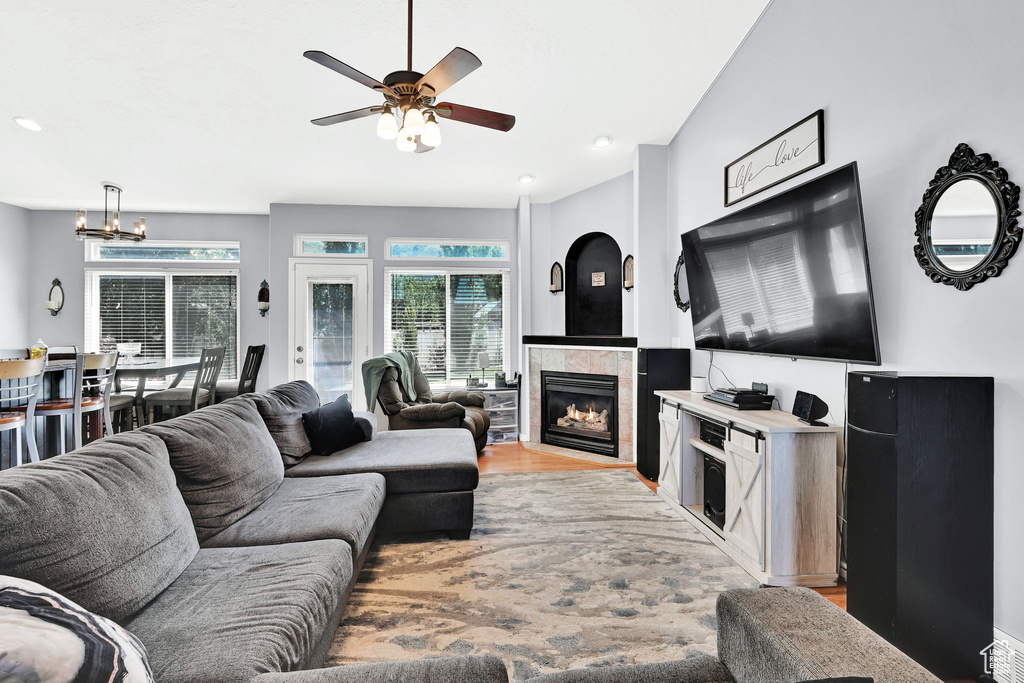 Living area with a ceiling fan, light wood-style flooring, a tiled fireplace, and a chandelier