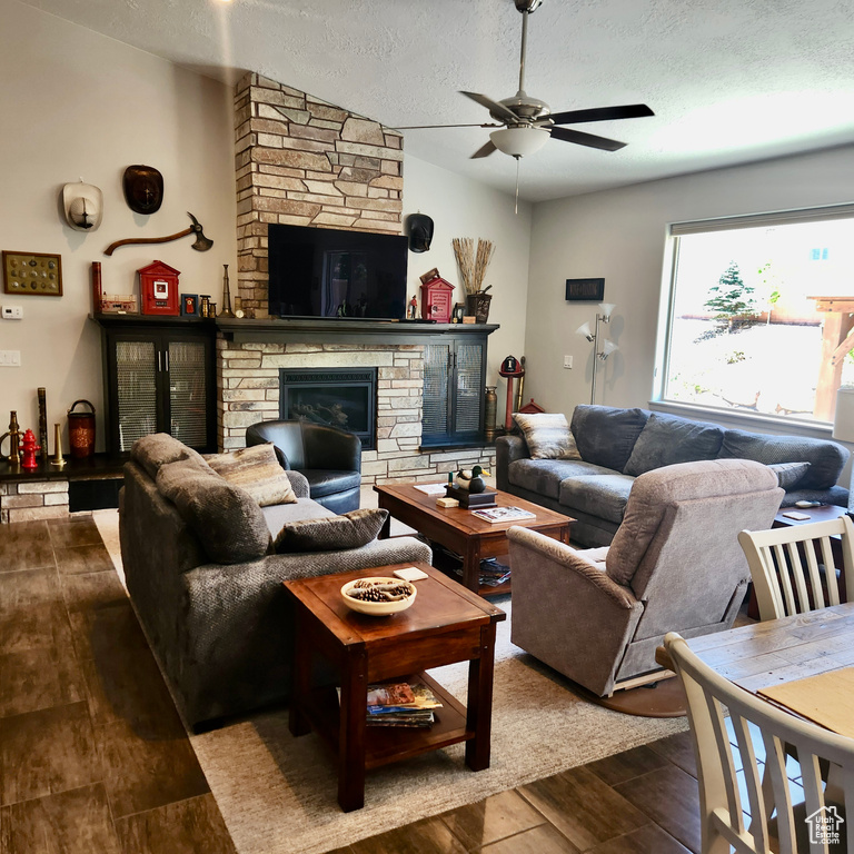 Living area featuring ceiling fan, a stone fireplace, dark wood-style floors, and a textured ceiling