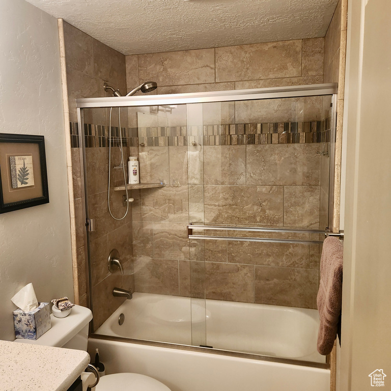 Bathroom featuring combined bath / shower with glass door, toilet, a textured ceiling, and vanity